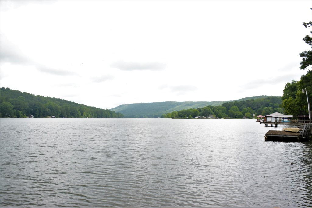 A lake with several small docks and homes visible around its shoreline, surrounded by forested hills.