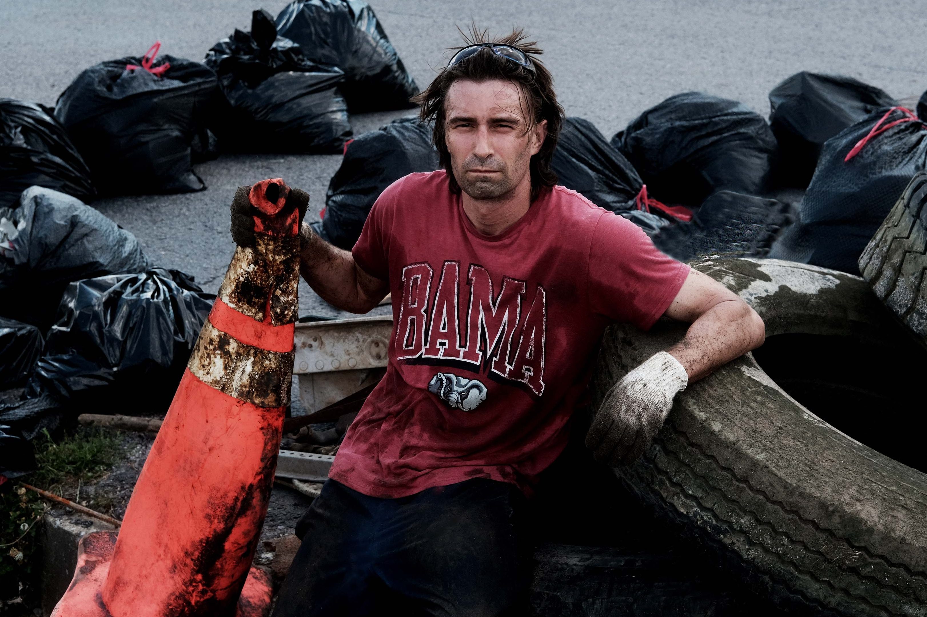 David Whiteside sits among garbage bags of collected litter, along with tires and a traffic cone, during a river cleanup.