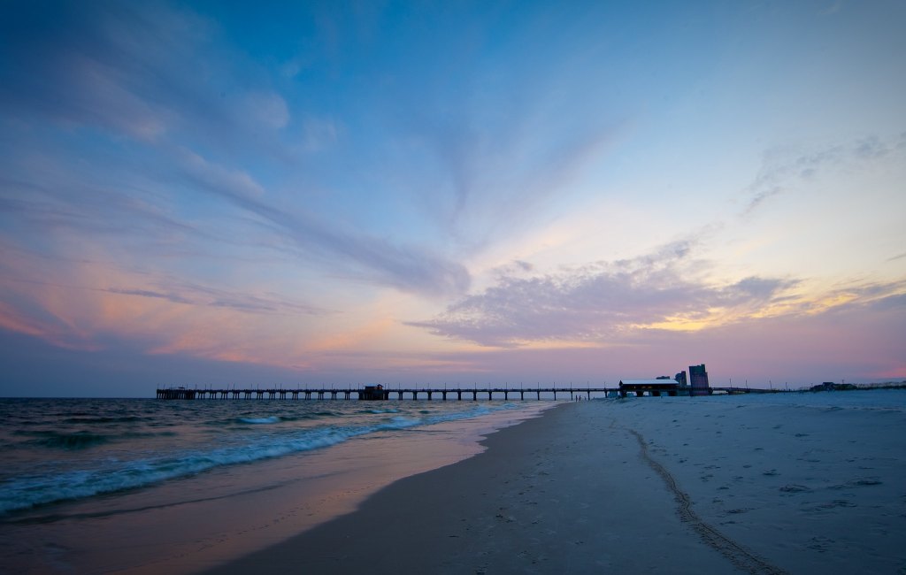 The beach at sunset, with a tall pier and hotels visible in the distance.