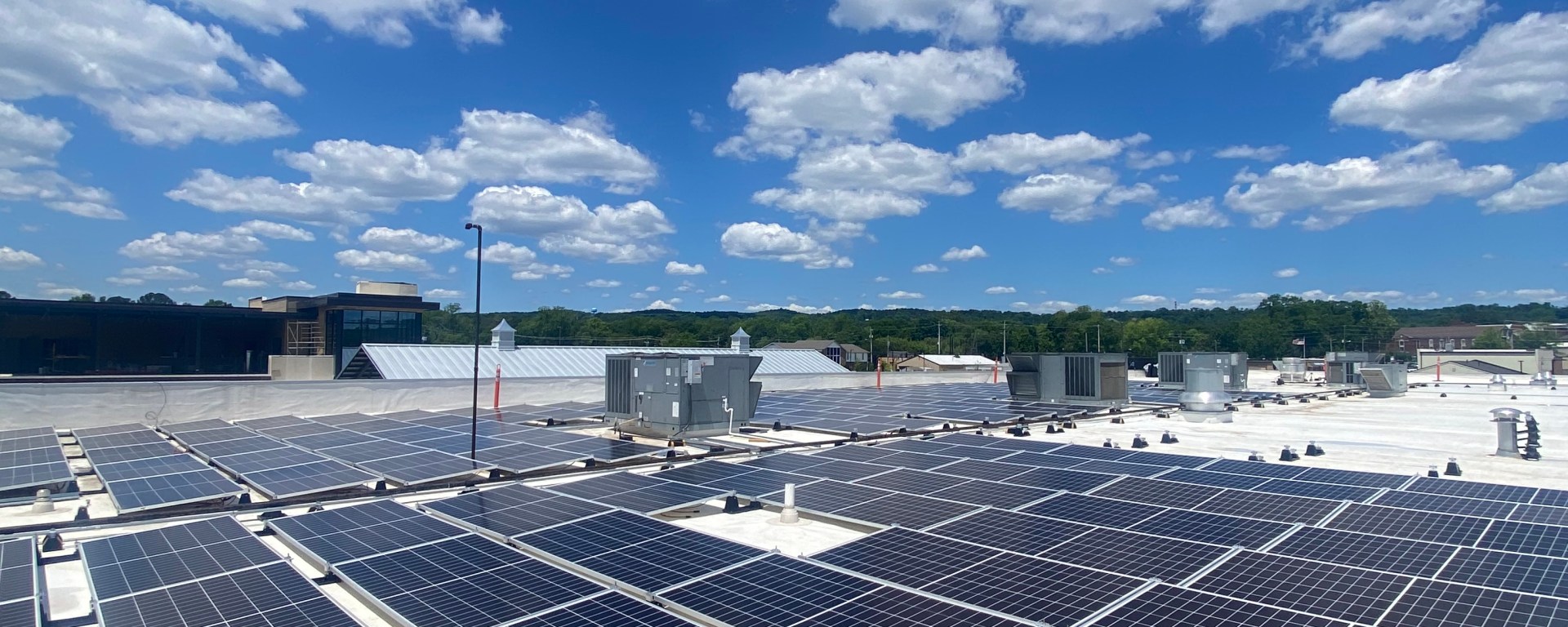 Rows of solar panels on top of a flat, white roof under a blue, slightly cloudy sky