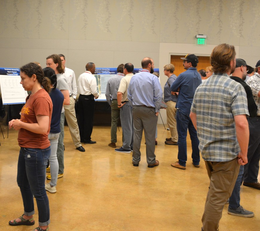 A meeting room is ringed with easels holding posterboards that describe various aspects of the fish passage project. People mill about the room to look at the boards and discuss with Army Corps of Engineers staff.