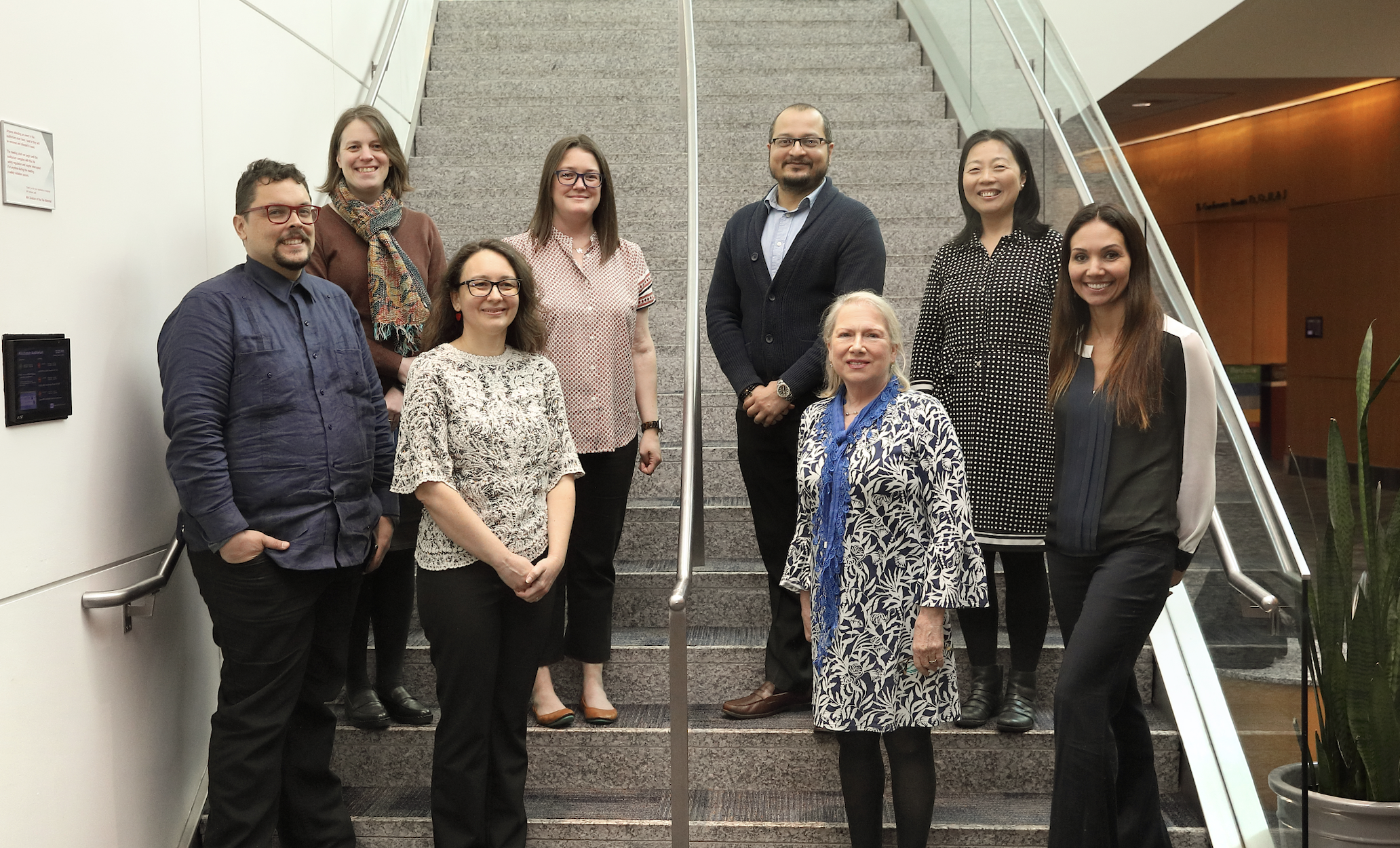 Eight people stand in two rows on a staircase. There are two men and six women.