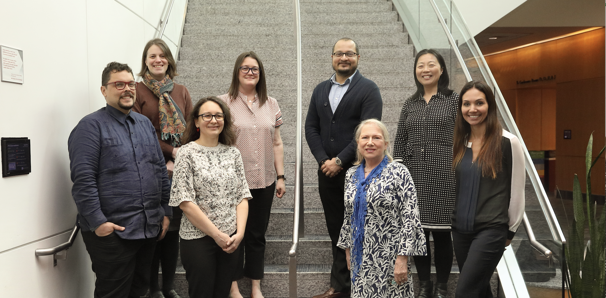 Eight people stand in two rows on a staircase.