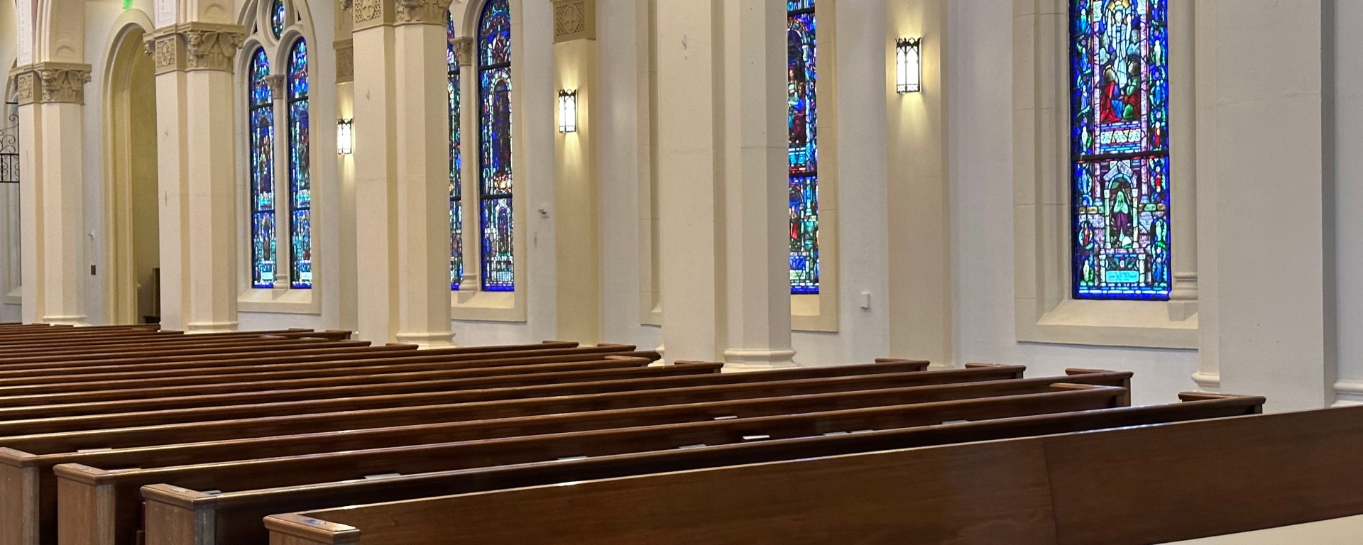 A row of wooden pews with stained glass and columns visible in the background.