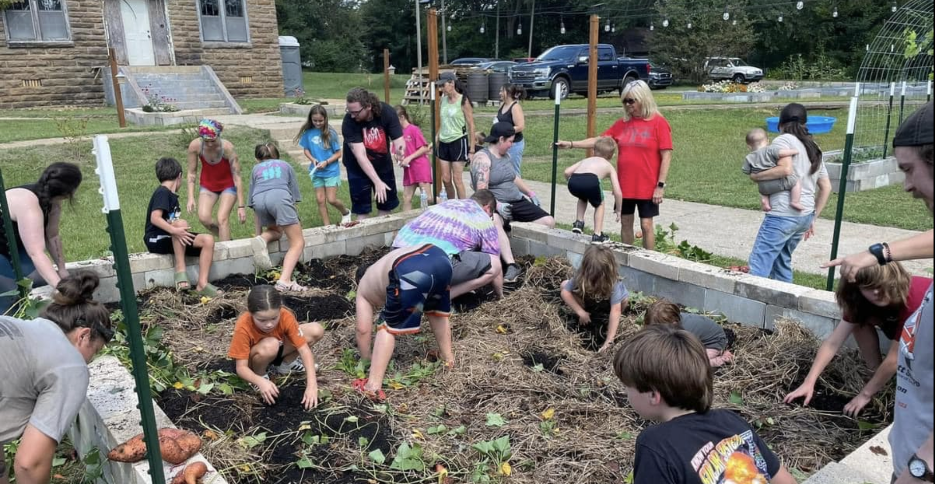 Children and adults surround a raised garden bed, built out of cinder blocks, where they are digging and doing other preparation work.