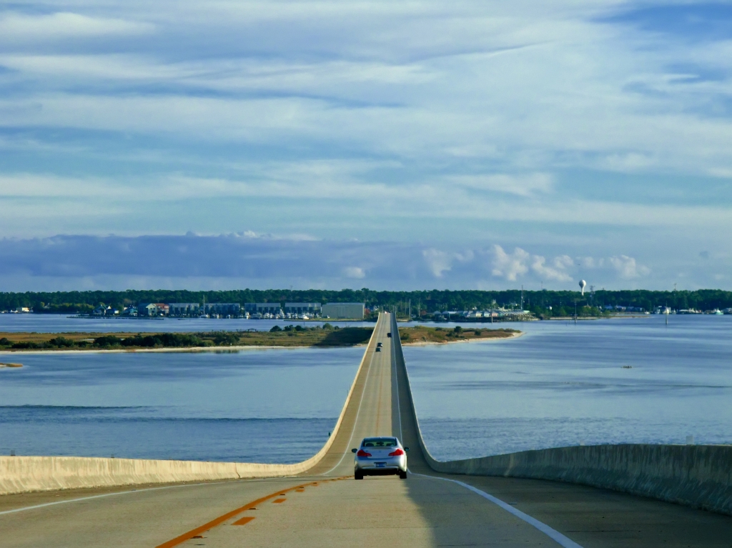 A view of the two-lane causeway from the front of a car. The highway is spanning the water, with land visible in the background.