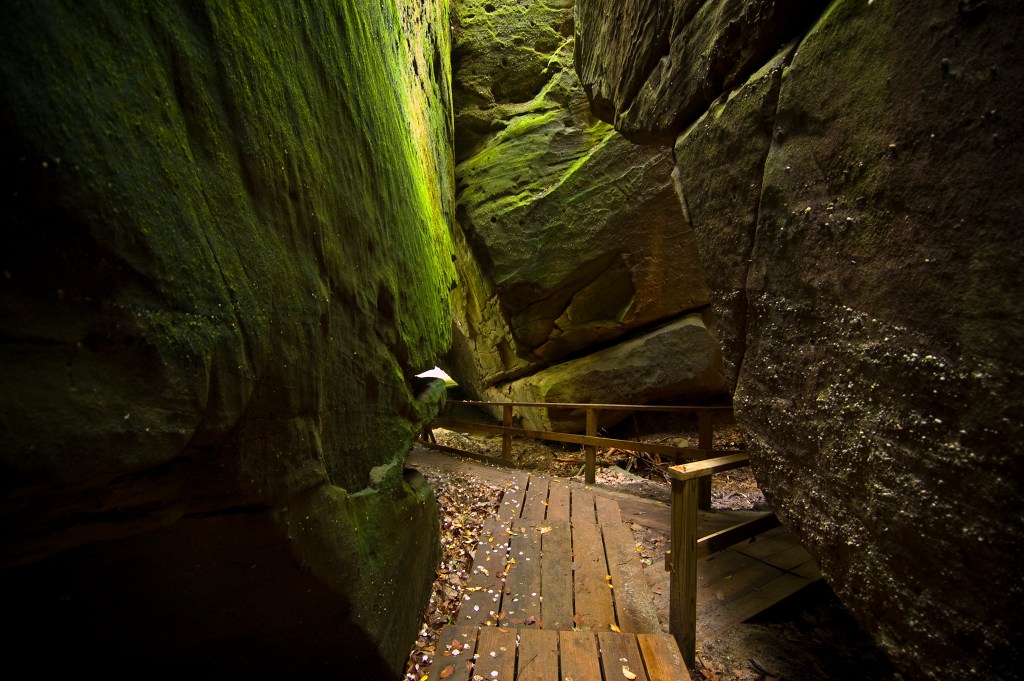 A wooden walkway with a railing between high, sheer walls of moss-covered rocks.